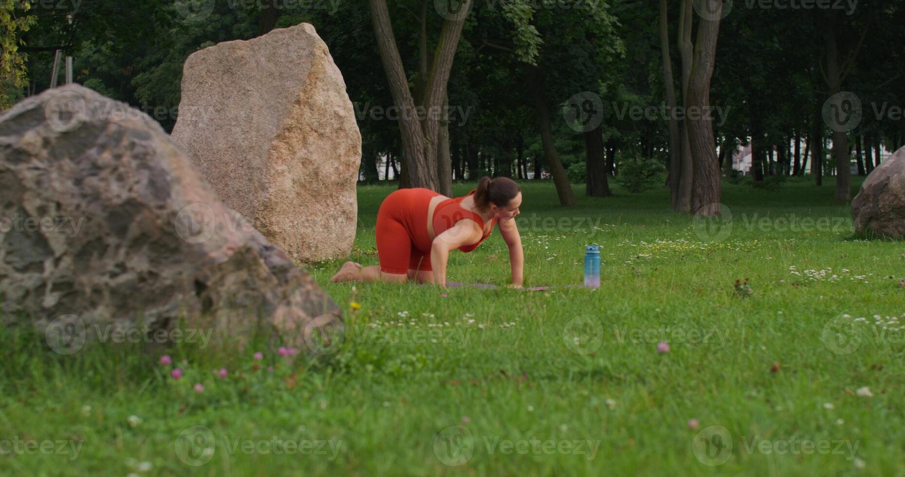 A pregnant woman in sports clothes does yoga on a sports mat in a city park on a summer day. The camera quickly changes its angle photo