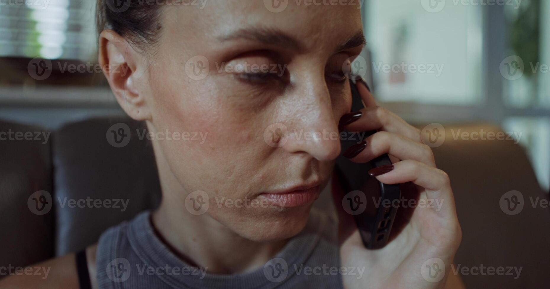 A woman is talking on a mobile phone while sitting at home. She shouts into the phone. Close-up of her face photo