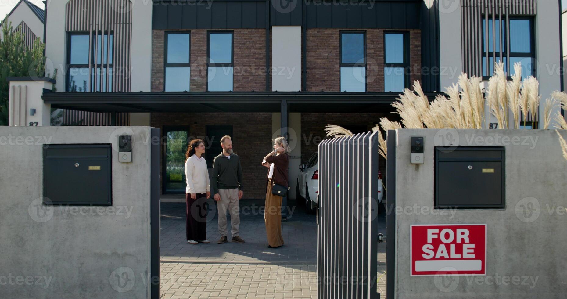 The realtor talks to the buyers of the house standing outdoors. Husband and wife look around photo