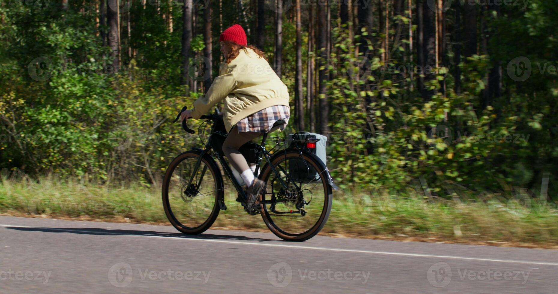 A woman rides a bicycle along the forest on a sunny day. Side view photo