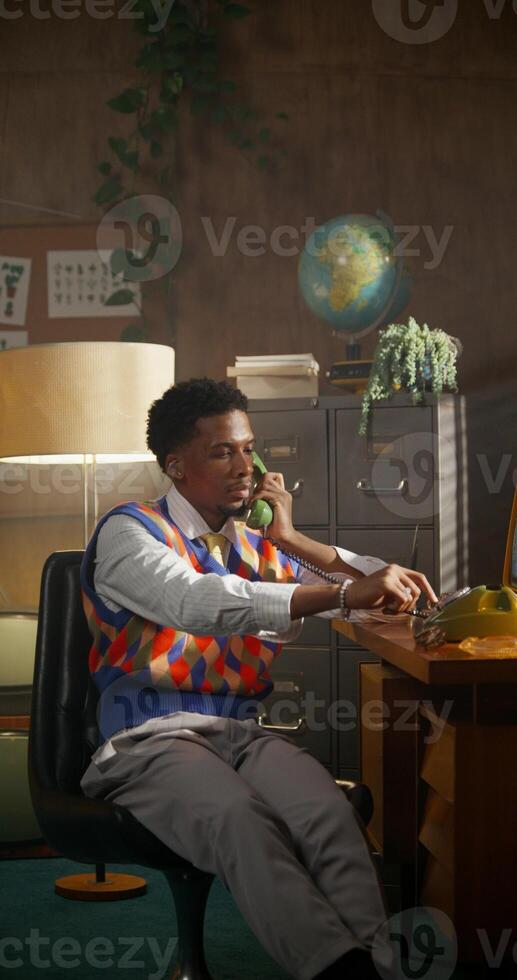 The man dials a number and starts a conversation on a wired phone. Working in a retro office. photo