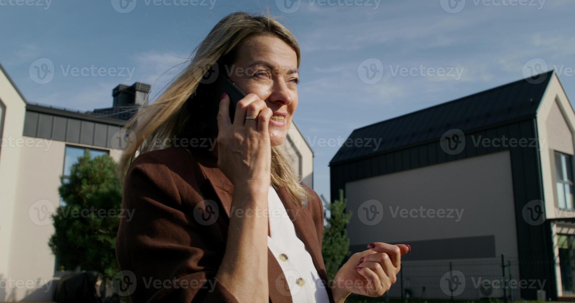 A woman smiles talking on a mobile phone while standing on a city street on a summer day. Close-up of her face photo