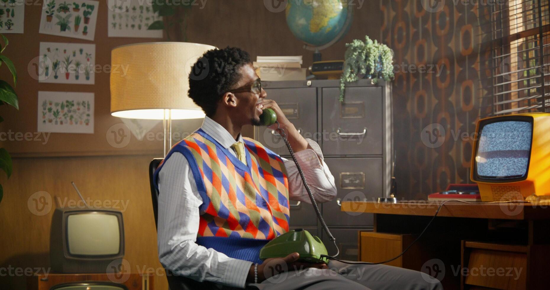 The man picks up the retro phone and talks emotionally with a wide smile. Old school office photo