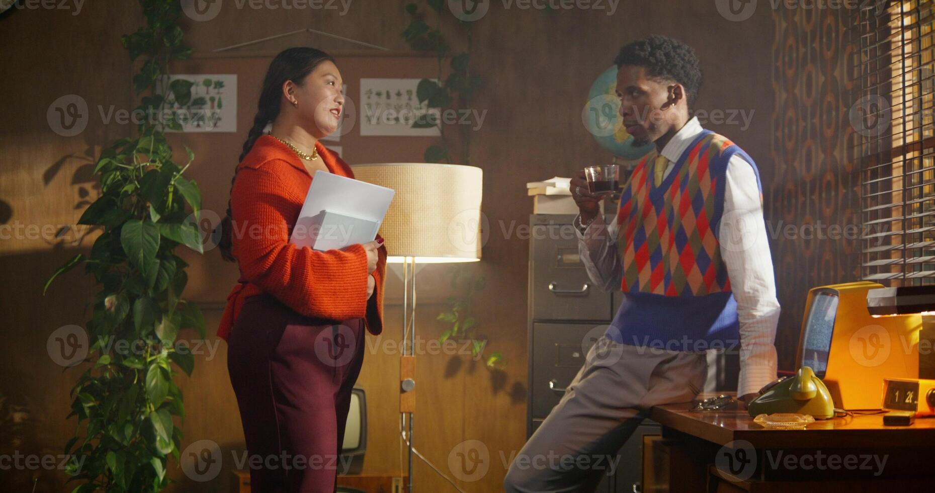 A man and a woman are talking standing in a retro office. A man is drinking coffee. A woman holds documents in her hands photo
