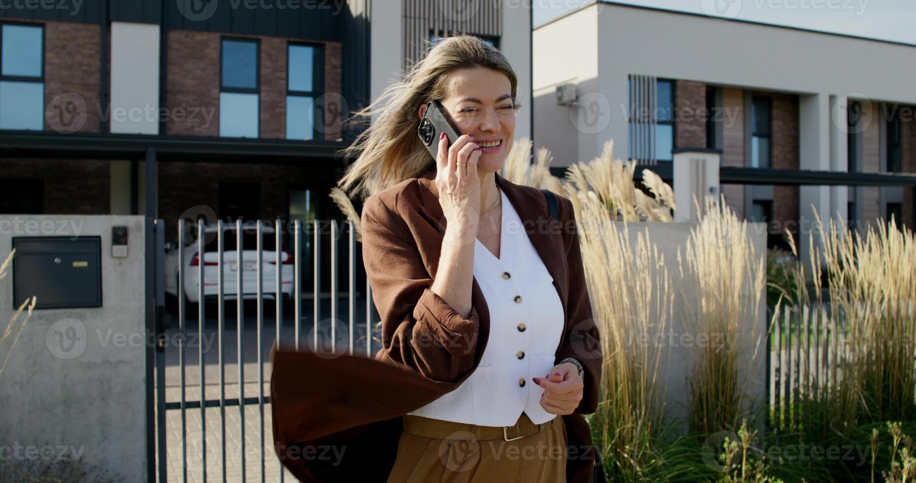 A business woman is talking on a mobile phone while standing near the house on a summer day photo