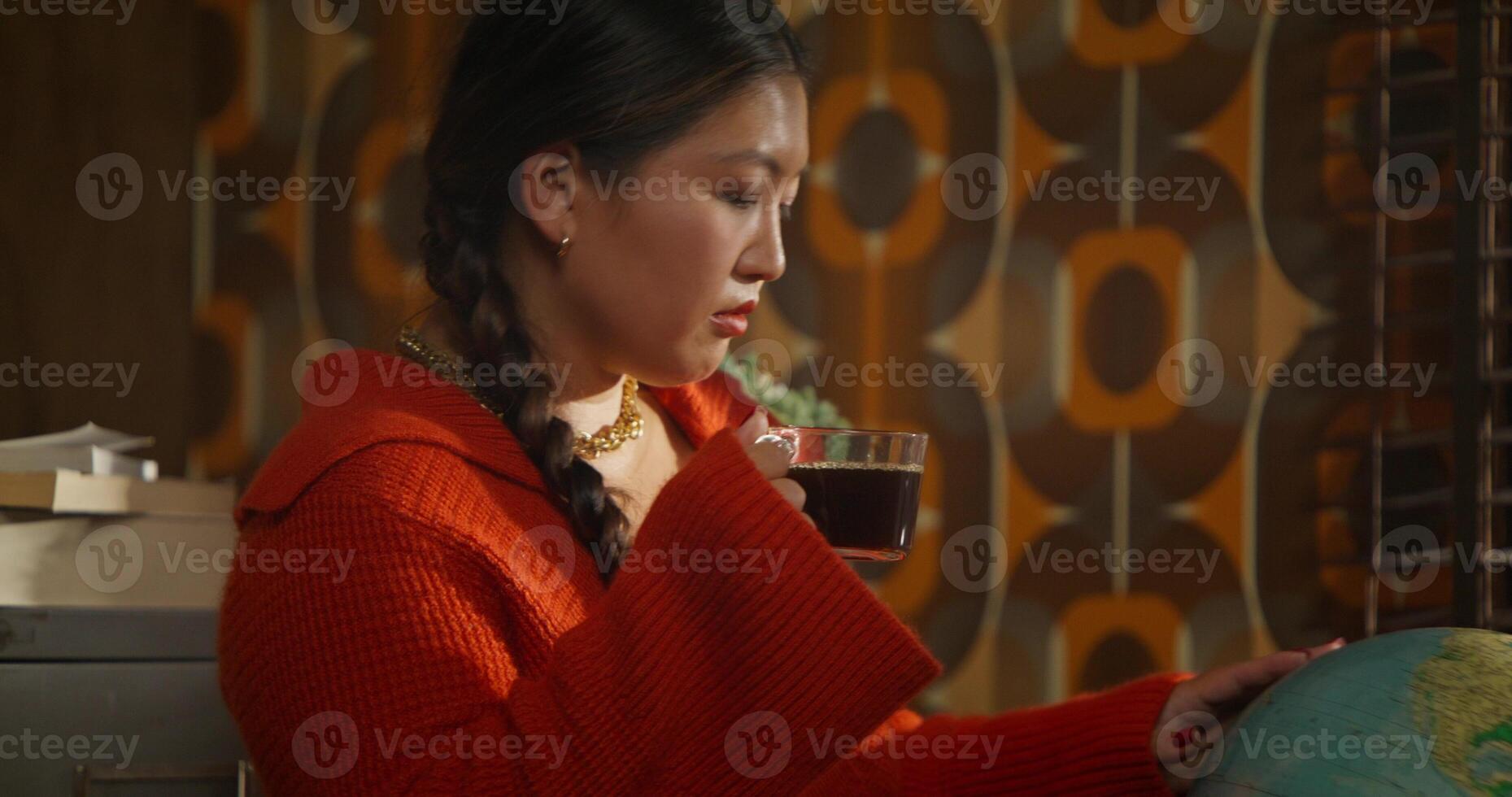 The woman turns the globe thoughtfully and drinks coffee. Retro office worker photo