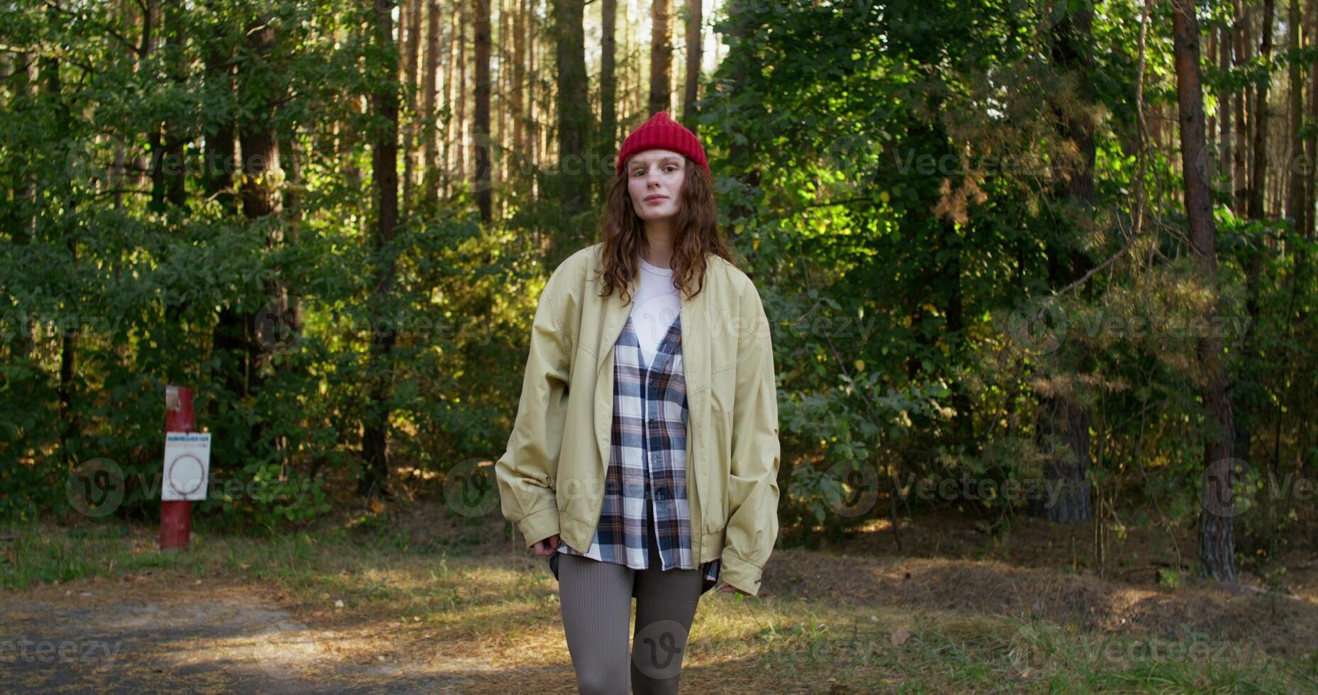 Portrait of a woman in the forest. She looks at the camera with a calm look standing on a forest path. A sunny, cool day photo