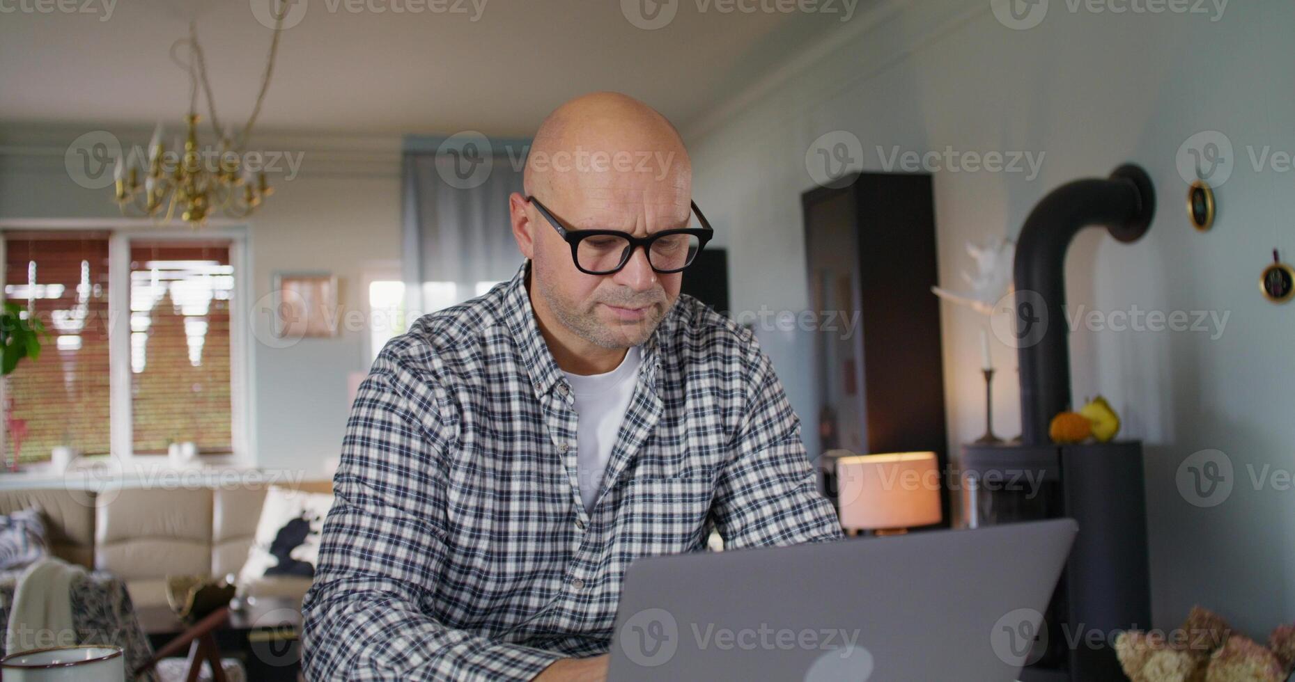 The man works from home. He uses a laptop and writes in a notebook with serious look photo