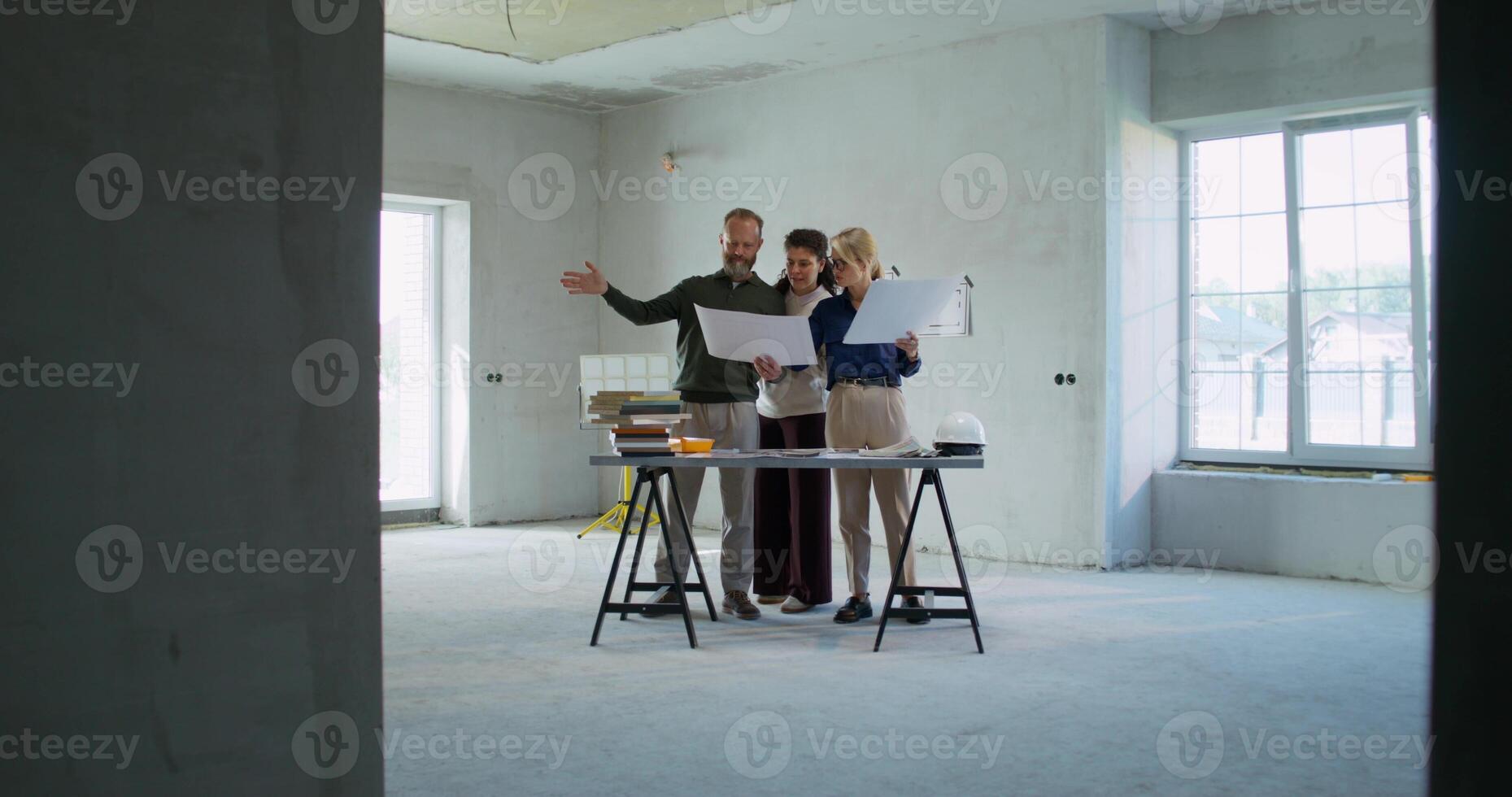The designer discusses the project with the customers, they consider the project of the house standing in a room without decoration photo