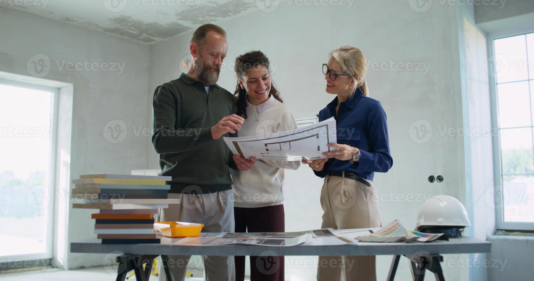 Happy customers discuss the design project of the house with the designer standing in a room without decoration photo