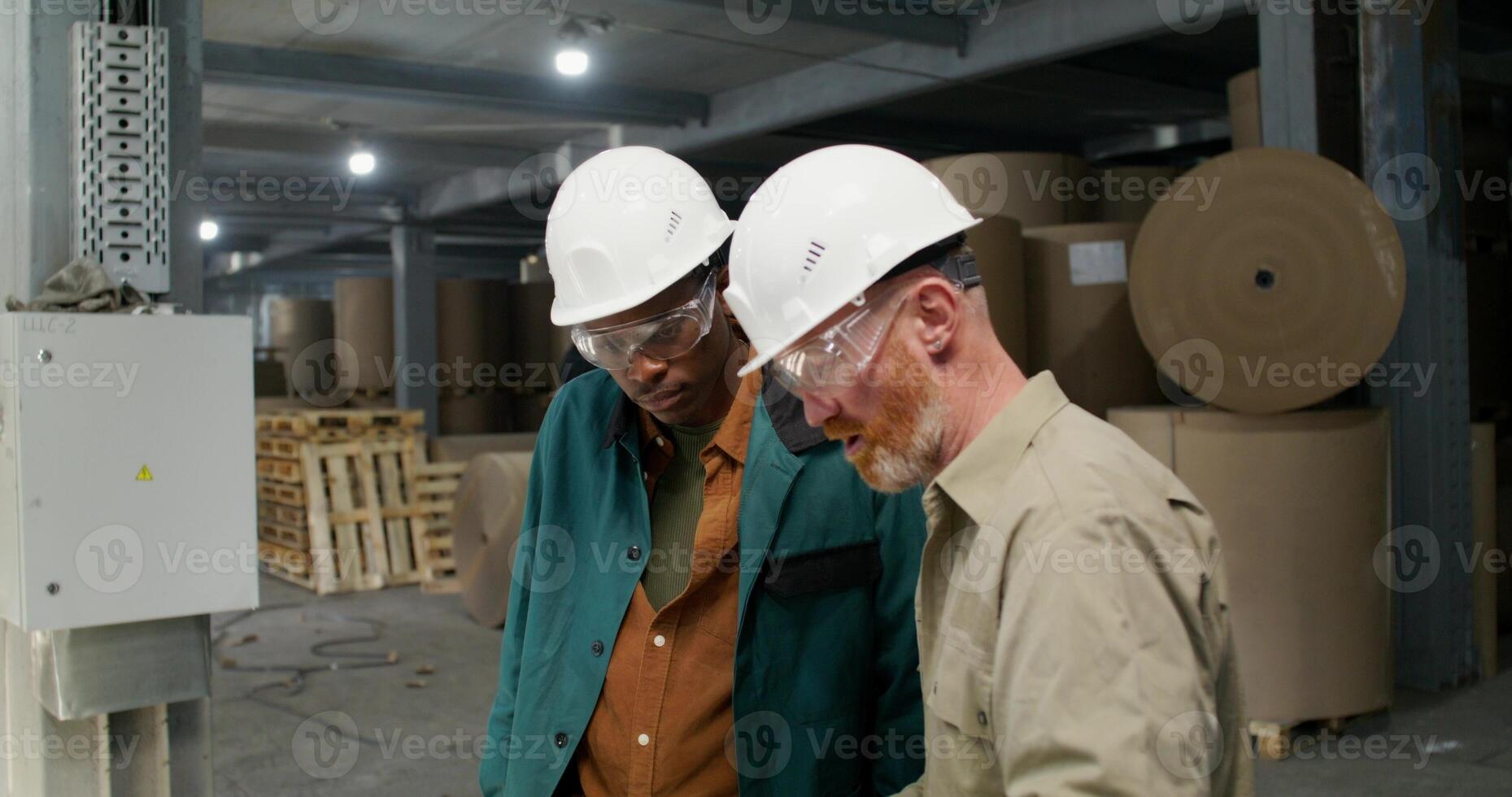 Two men in protective helmets and glasses are talking standing in a paper mill photo