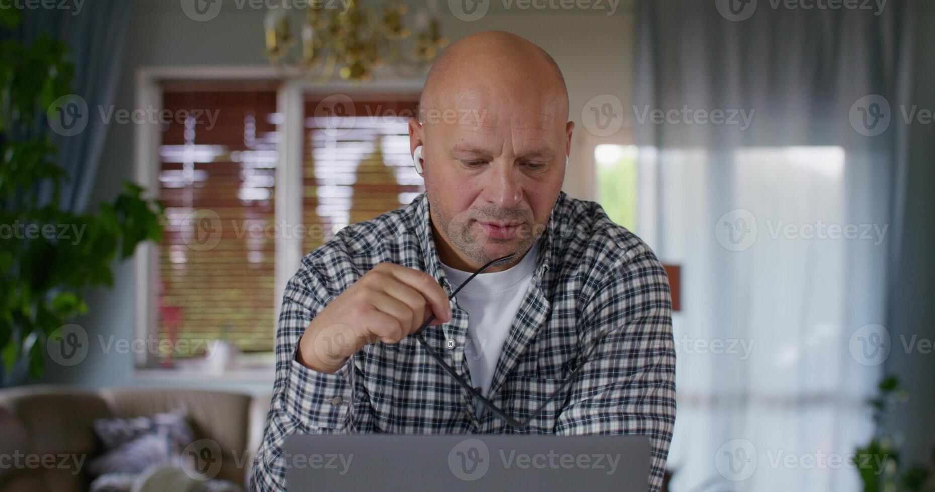 A man thinks while working on a laptop. He's sitting at the kitchen table at home photo