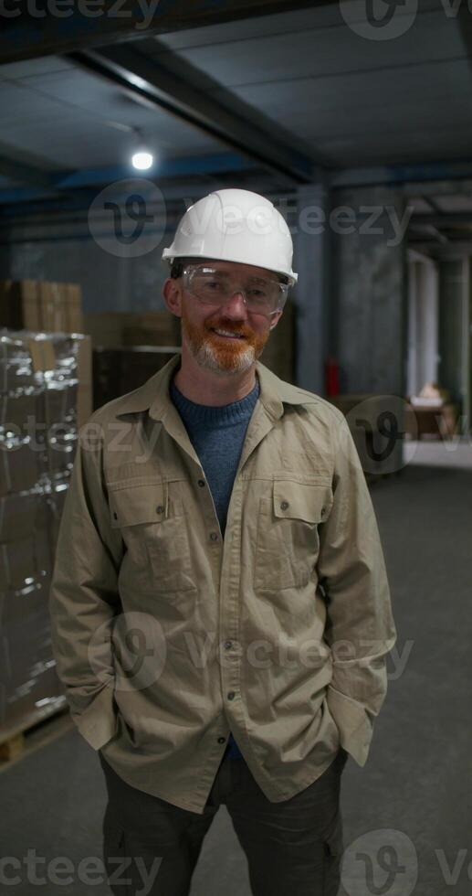 A man in a work uniform is smiling at the camera. He is in the factory warehouse photo