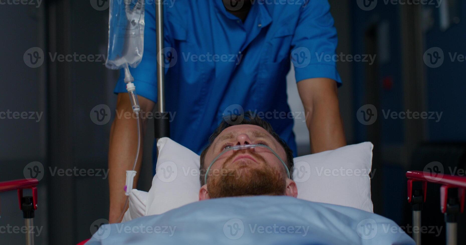 An orderly carries a patient with an oxygen tube in his nose on a trolley along the hospital corridor photo