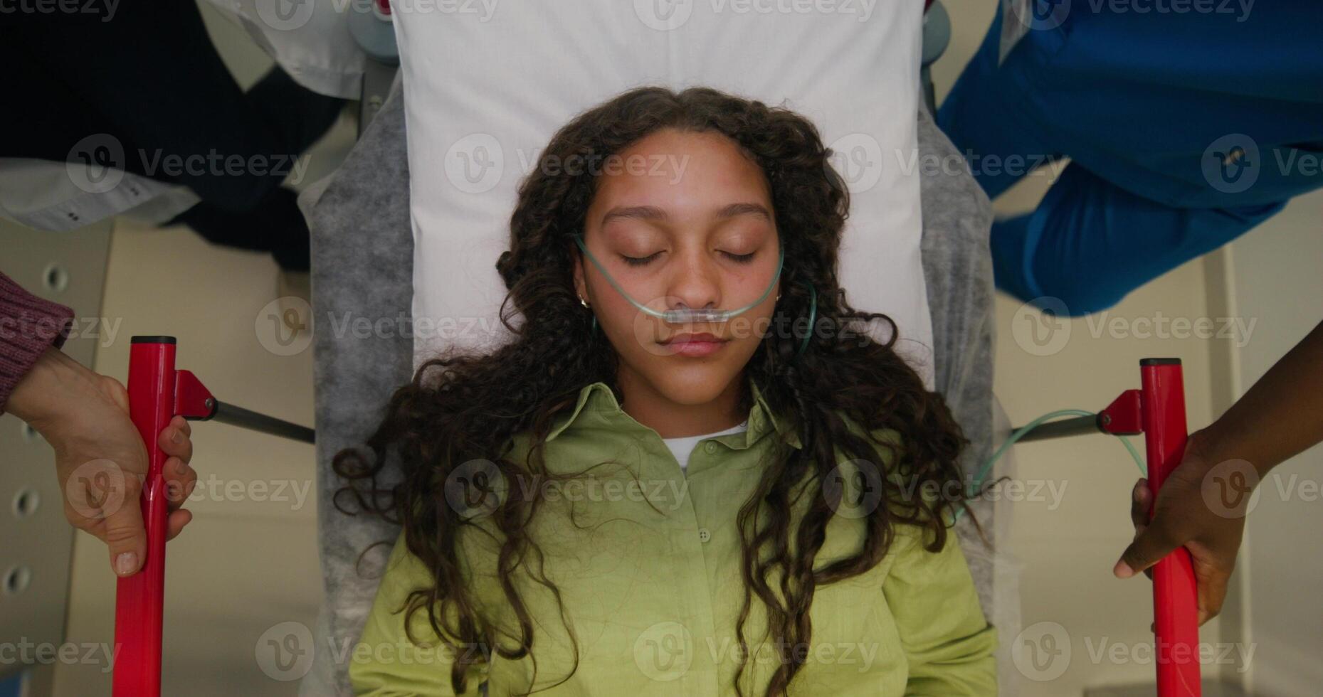 A woman with a breathing tube in her nose is lying on a gurney, top view. She is being driven down the hospital corridor, her eyes are closed photo