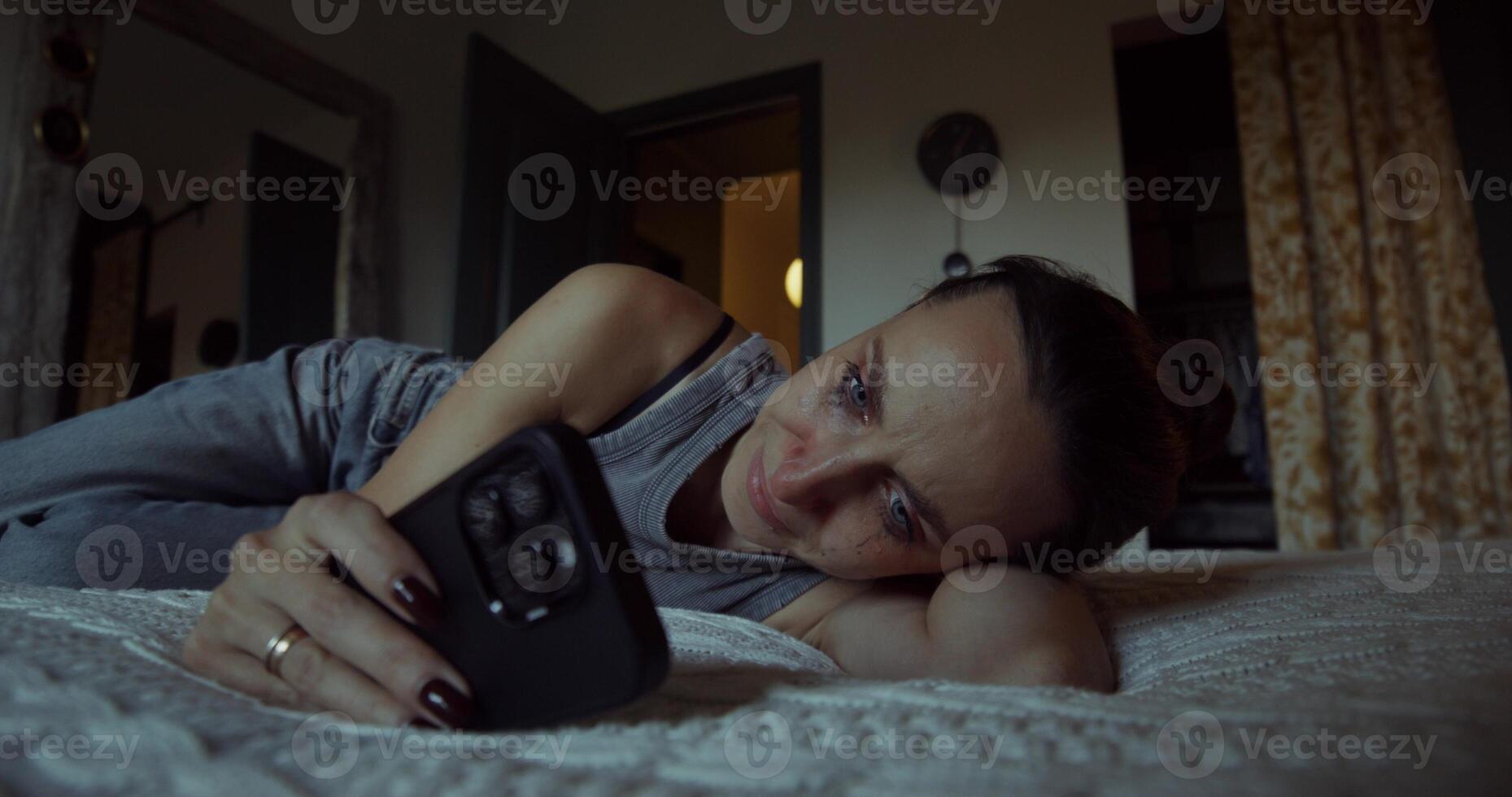 A woman cries when she uses a mobile phone. Her mascara was leaking. She's lying on the bed at home photo