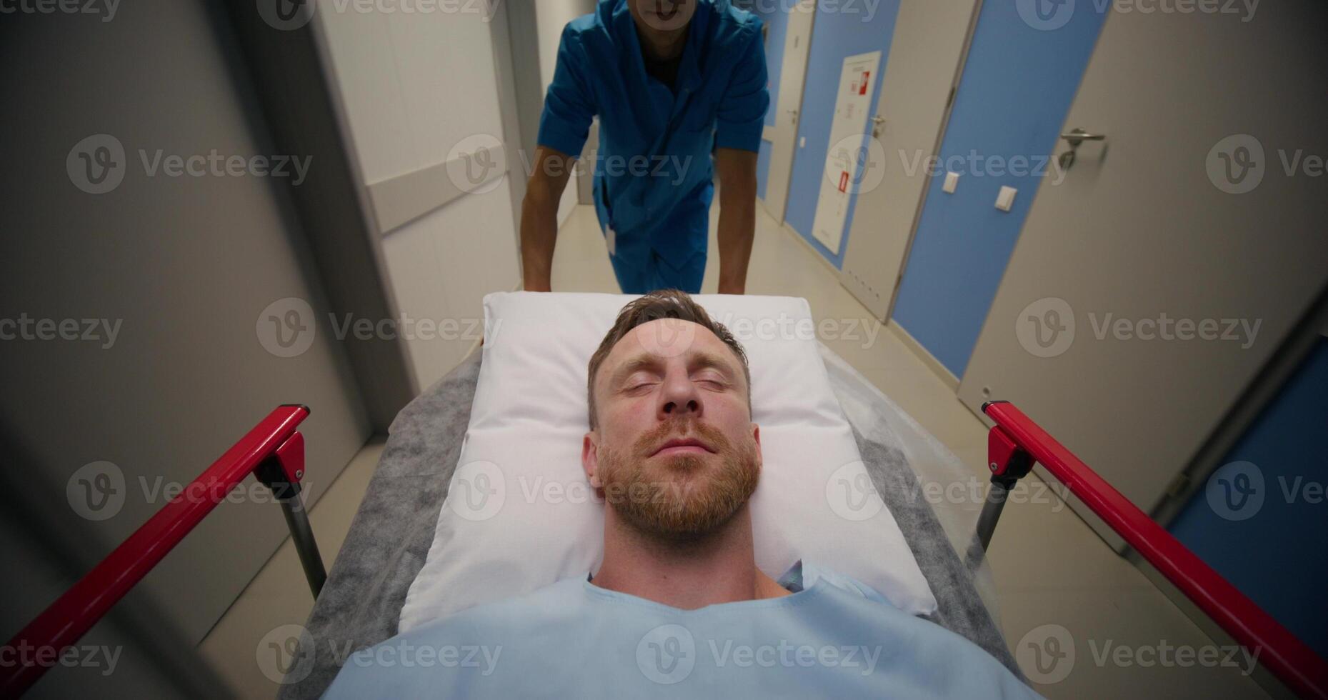 A man is lying on a medical gurney, he is being driven through a hospital corridor, his eyes are closed photo