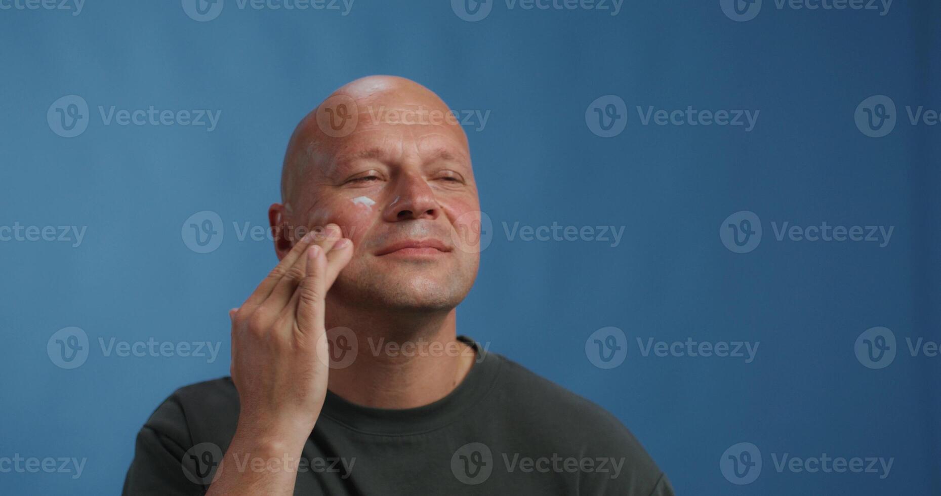 A bald man with a black shirt is touching his face photo