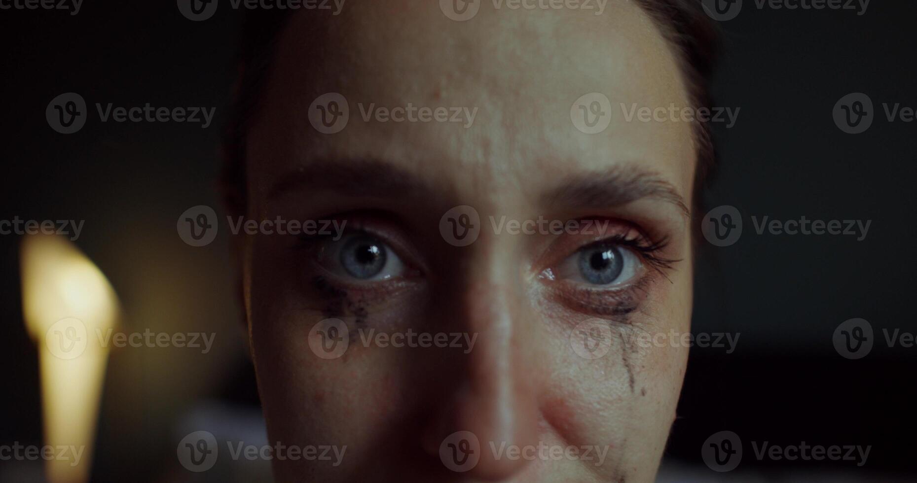 A woman is crying sitting on a bed at home. Her mascara was leaking. She's looking at the camera. Close-up of her face photo
