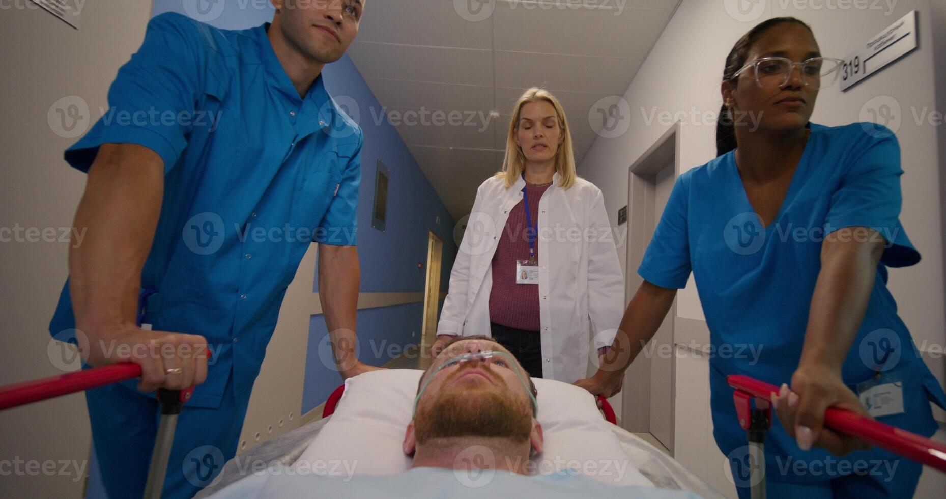 A man with an oxygen tube in his nose is lying on a medical gurney. The doctor talks to the paramedics as they take the patient through the hospital corridor photo