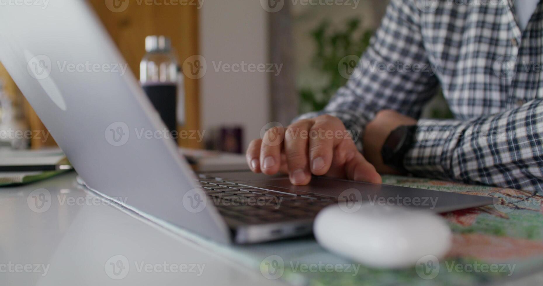 A man is typing on a laptop while sitting at the kitchen table at home. Close-up of his hands, an unrecognizable person photo