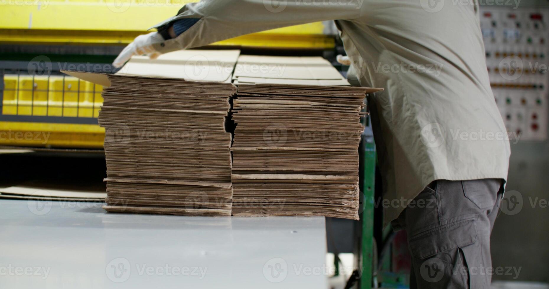 A man in a hard hat works at a paper mill. He picks up the machine-cut cardboard with a concentrated look photo
