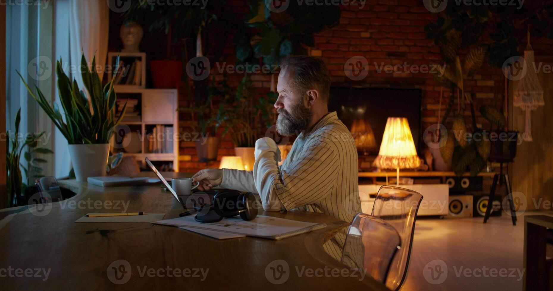 A respectable man with a beard typing on a laptop while sitting at a desk at home. Night work. Remote workplace photo