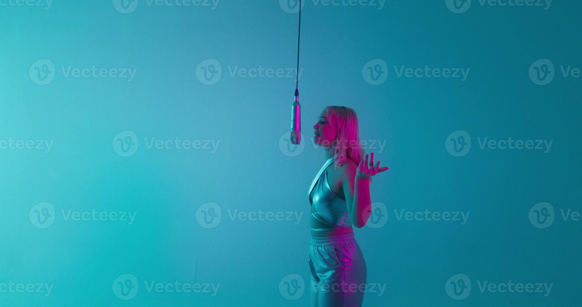 A glamorous woman sings into a microphone. Recording clip in the studio. The camera zooms from the general plan to the singer's face photo