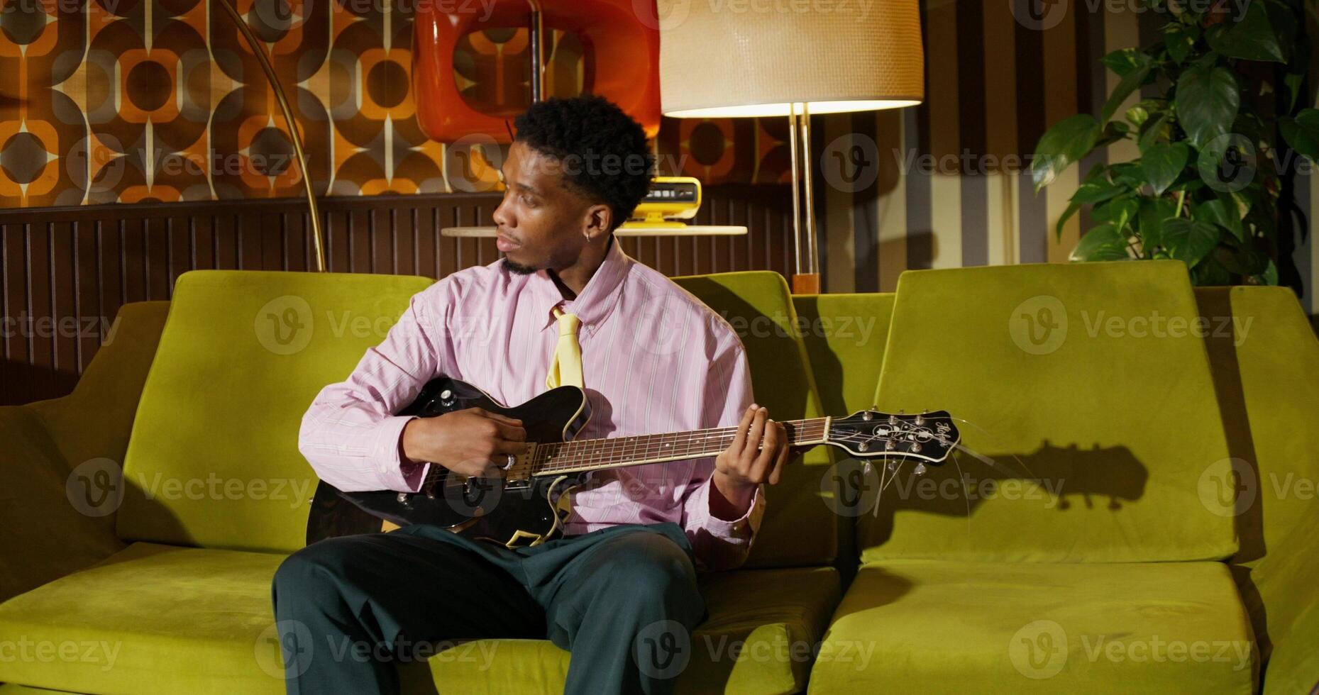 A man plays the guitar at home. He is sitting on a sofa in a retro interior and smiling photo