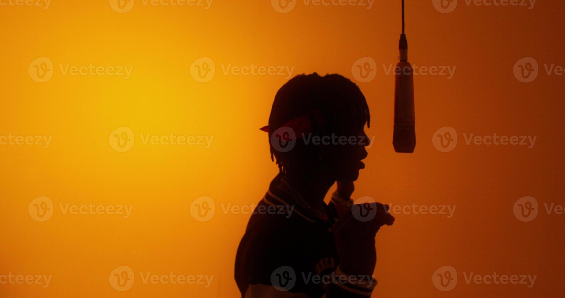 A stylish young man sings into a hanging microphone. Studio on an orange background photo