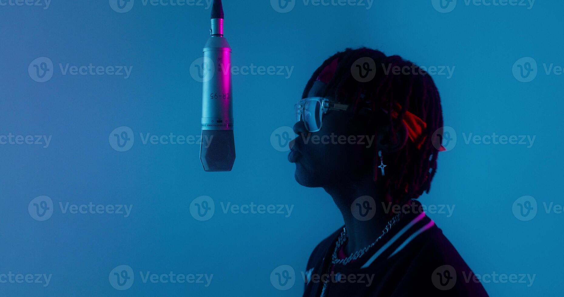Recording a clip. The rapper sings into a hanging microphone standing on a blue background in the studio photo