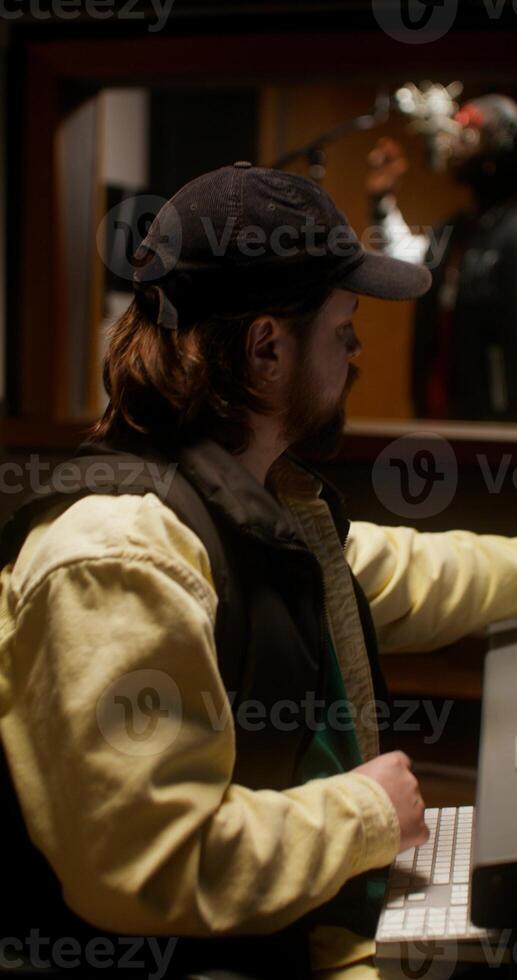 The sound engineer controls the recording process of the song in the studio. Close-up of his face. The rapper sings in the room behind the glass photo