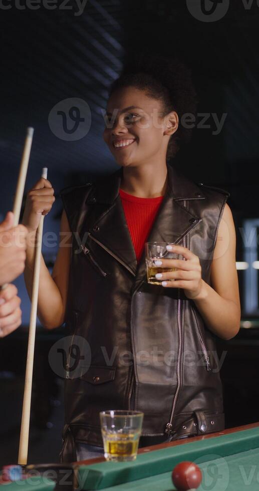 A young man of European appearance and an African-American woman are playing billiards, talking and drinking beer. Fun pastime with talking and playing. vertical photo