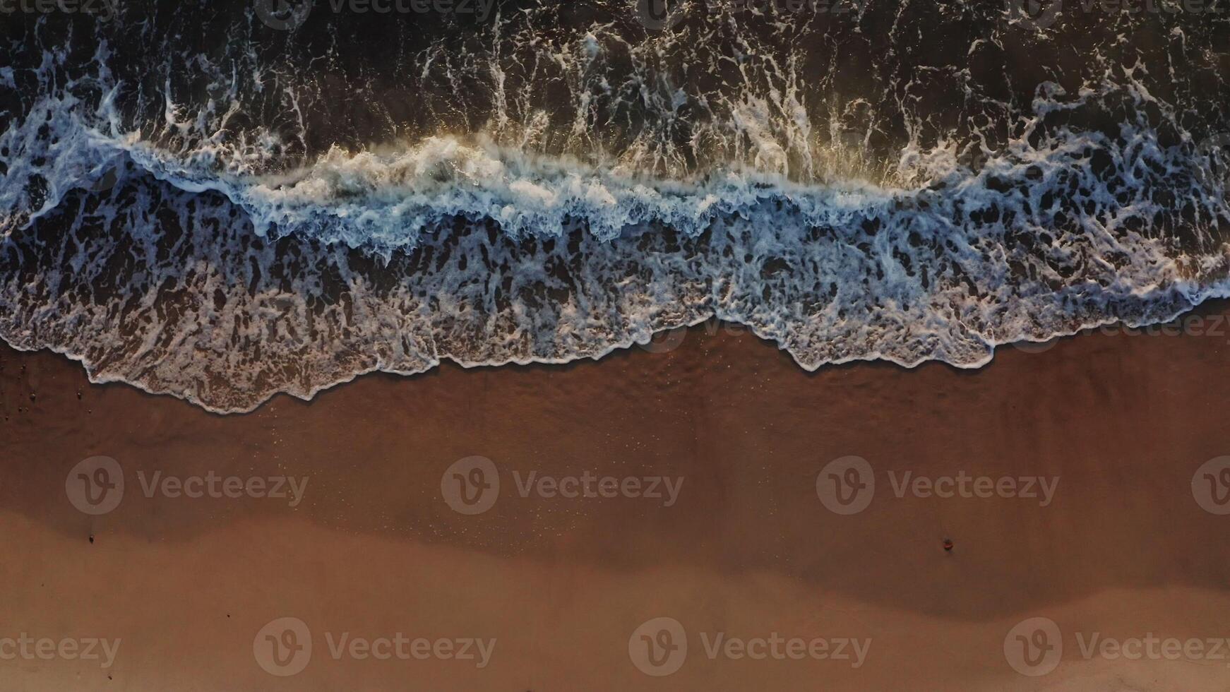 Top view from a drone on the coastline. Sea waves wash the sandy beach. Foamy water washes the sand in beautiful patterns, a bird's-eye view. No people. photo
