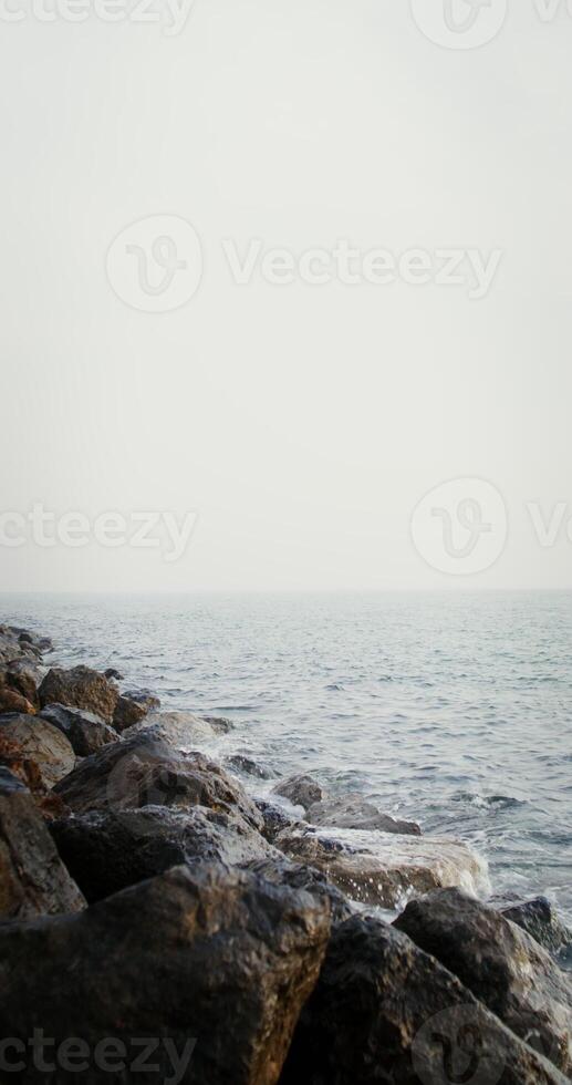 Sea waves hit large rocks on the coast, splashing and spraying in different directions. Vertical on a sunny day. 4k , red komodo photo