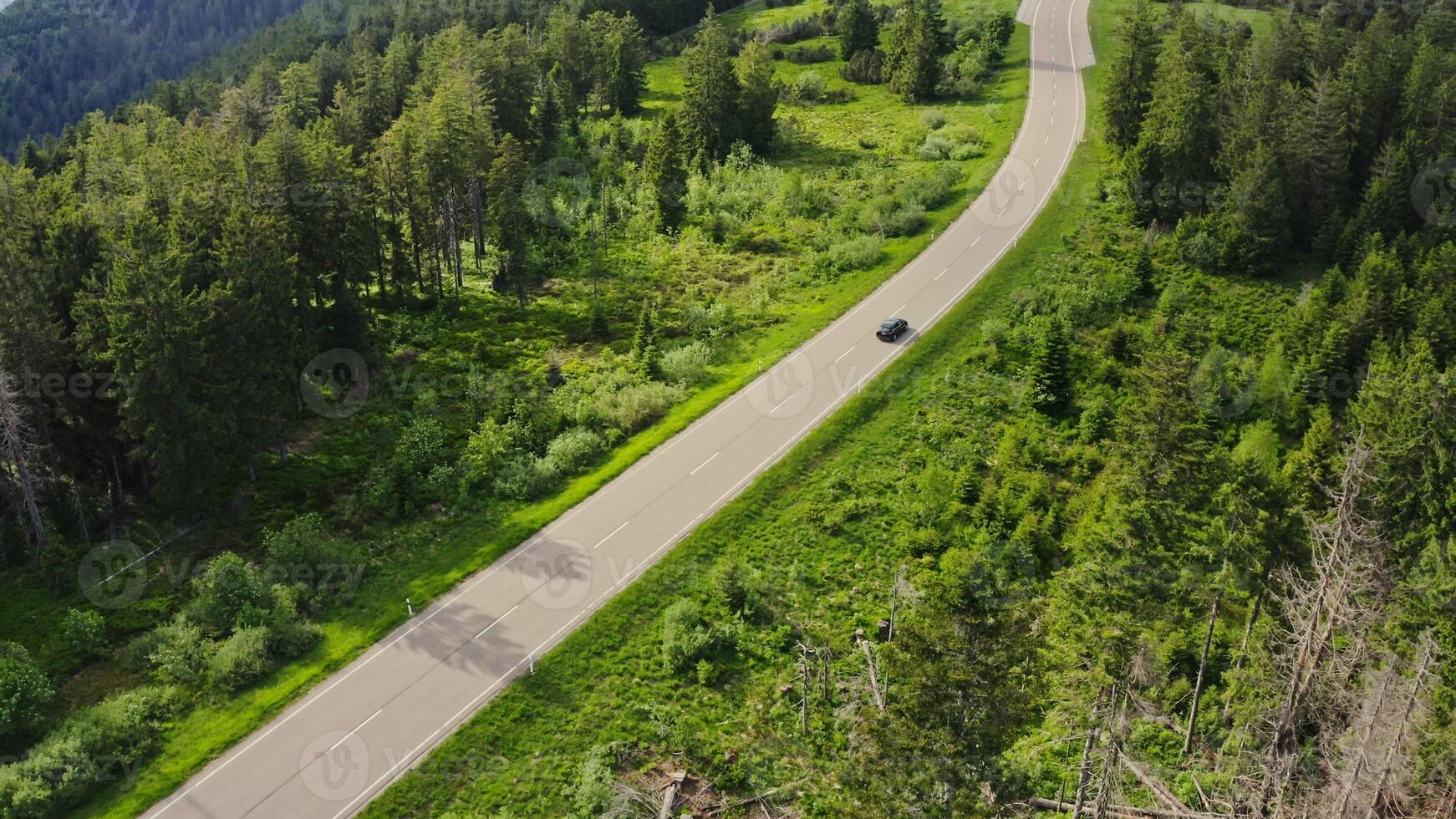 The car is driving on a mountain road, from a drone. Gentle slopes overgrown with dense spruce forest. Green valley from a bird's eye view photo