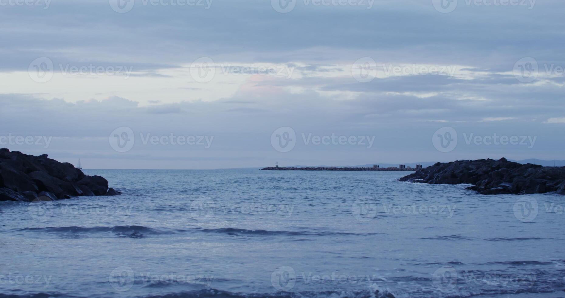 A lighthouse and a sailboat in the distance at sea among rocky ledges. Coastal reefs in the sea or ocean, washed by waves. in 4k, red komodo. photo