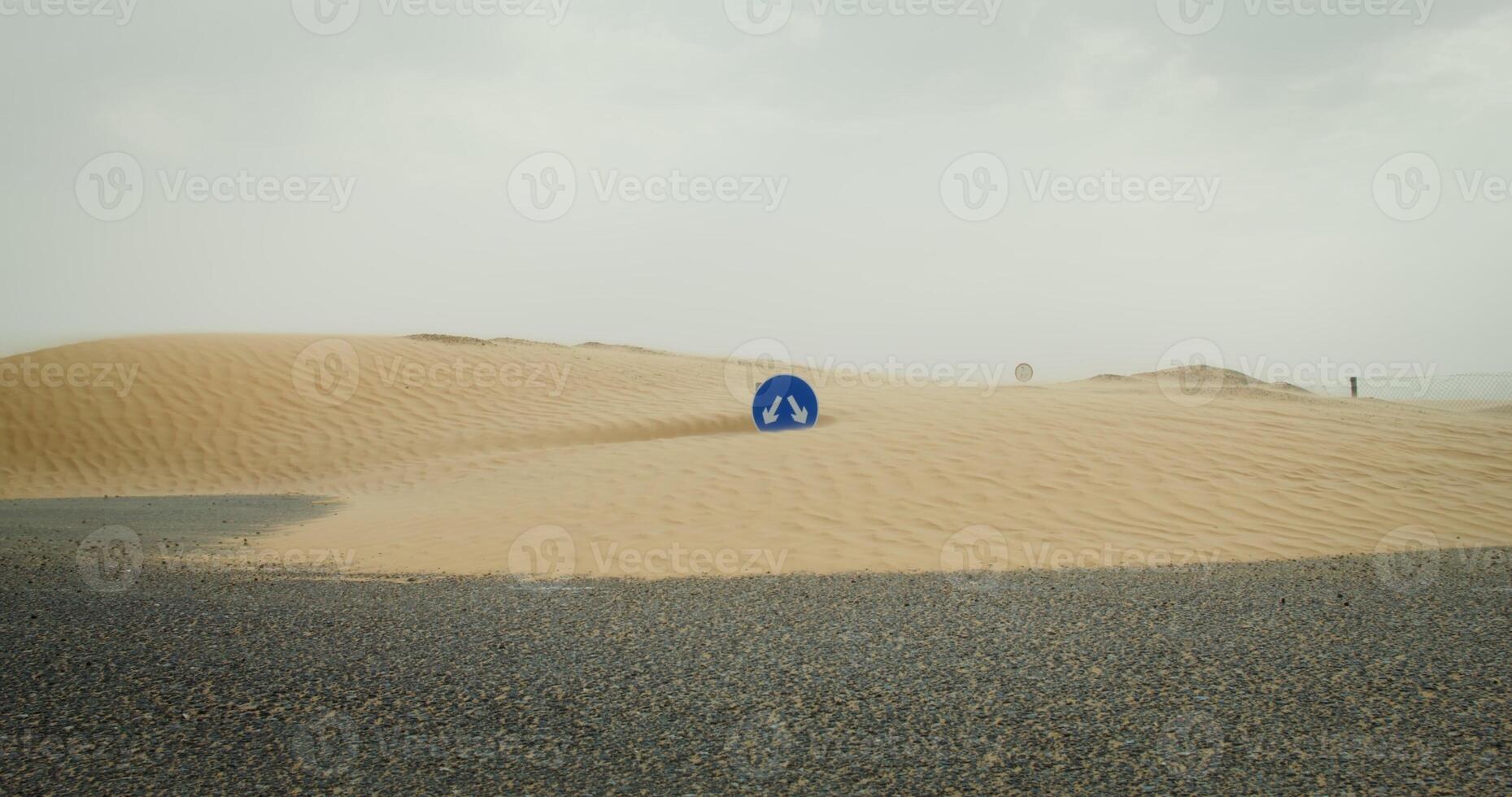 Asphalt road covered with desert sands. The road sign is practically buried under the yellow sand. The wind develops fine sand dust. 4k , red komodo photo