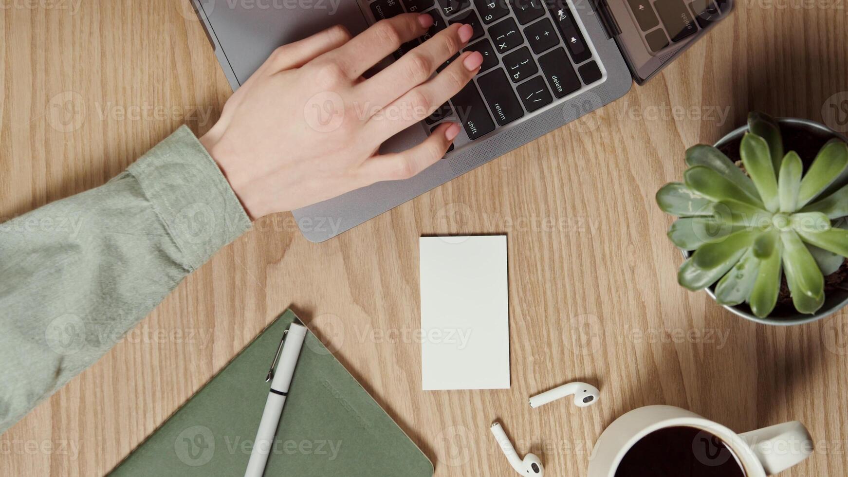 A white paper the size of a business card lies on the desktop of a young woman typing on a laptop. Close-up of female hands, no face. vertical . Place to copy. in 4k, red komodo photo