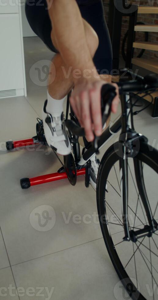 A young man in headphones with a towel around his neck uses an exercise bike while exercising at home, moves from the man's legs to his face photo