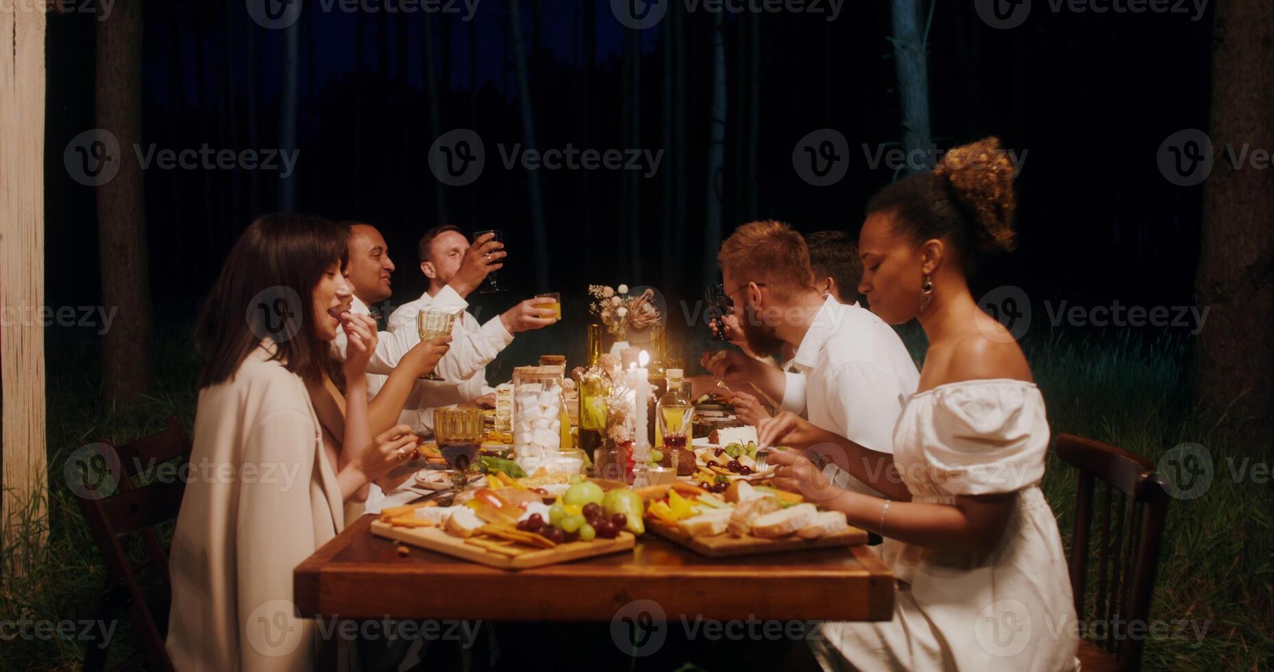 Guests smile and talk while eating sitting at a festive table outdoors at night photo