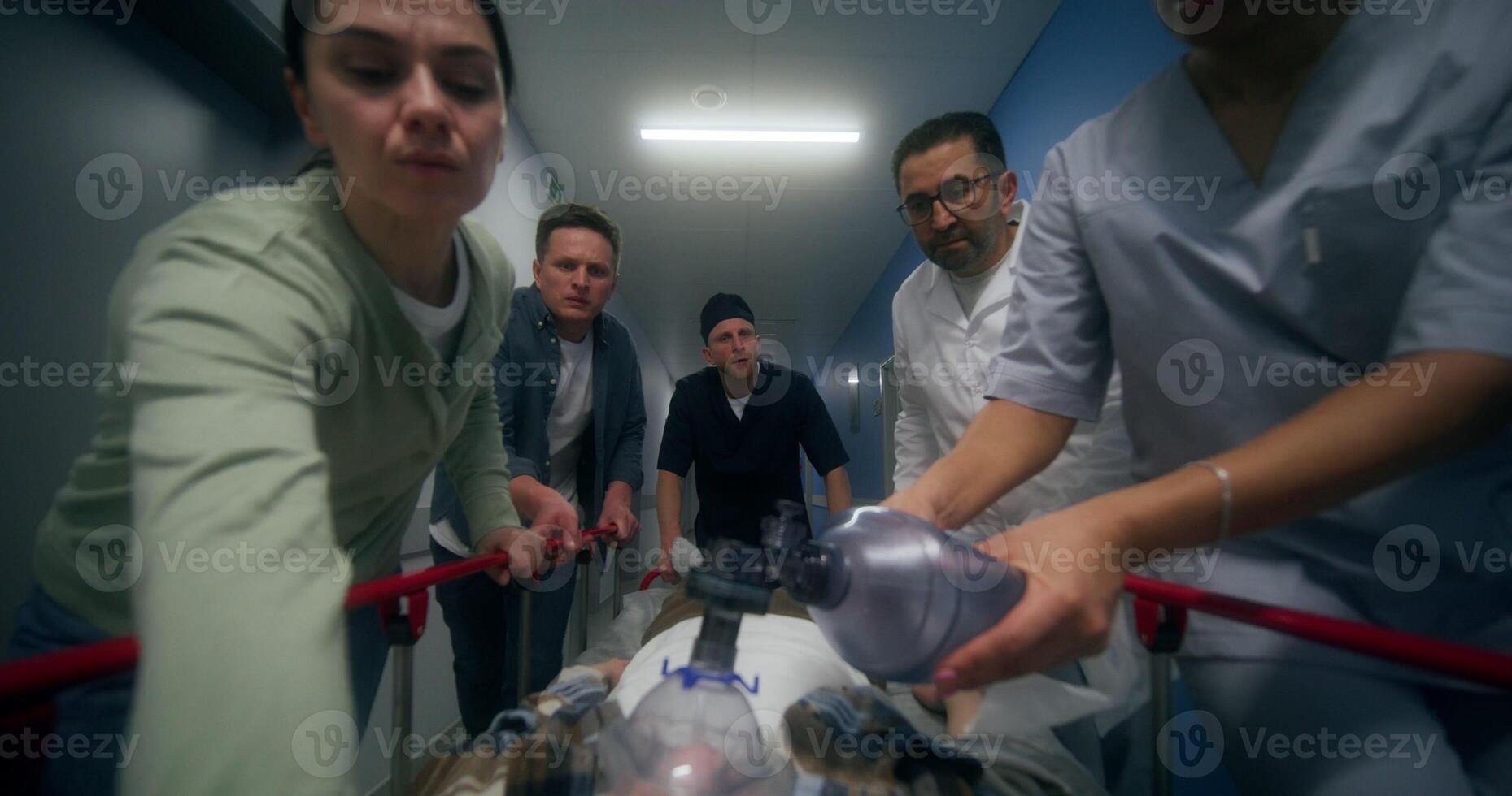Medical staff and relatives of the victim are running down the hospital corridor carrying the patient on a gurney, giving him oxygen through a mask photo