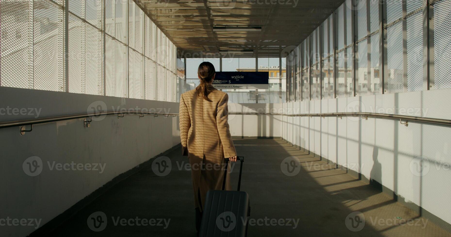 A woman in a coat with luggage in her hand walks through the railway station, rear view, unrecognizable person photo