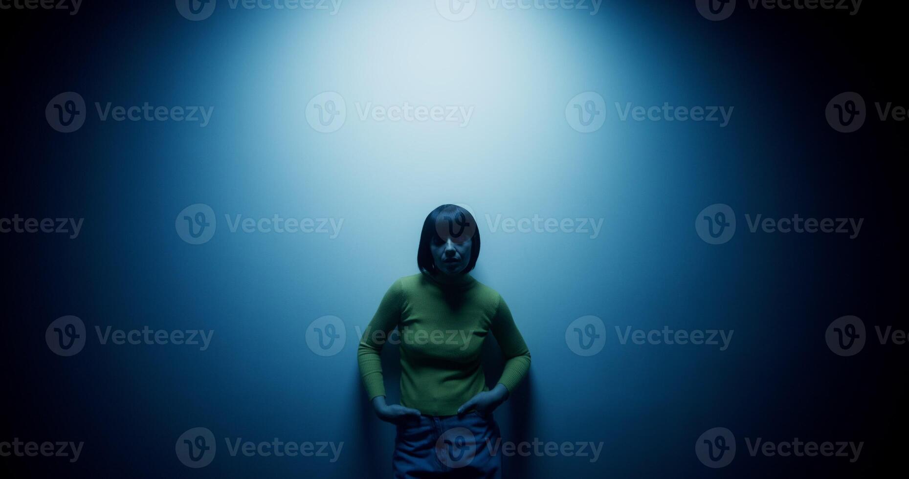 A woman in a wig is leaning against the wall posing in the blue light of a lamp in the studio photo