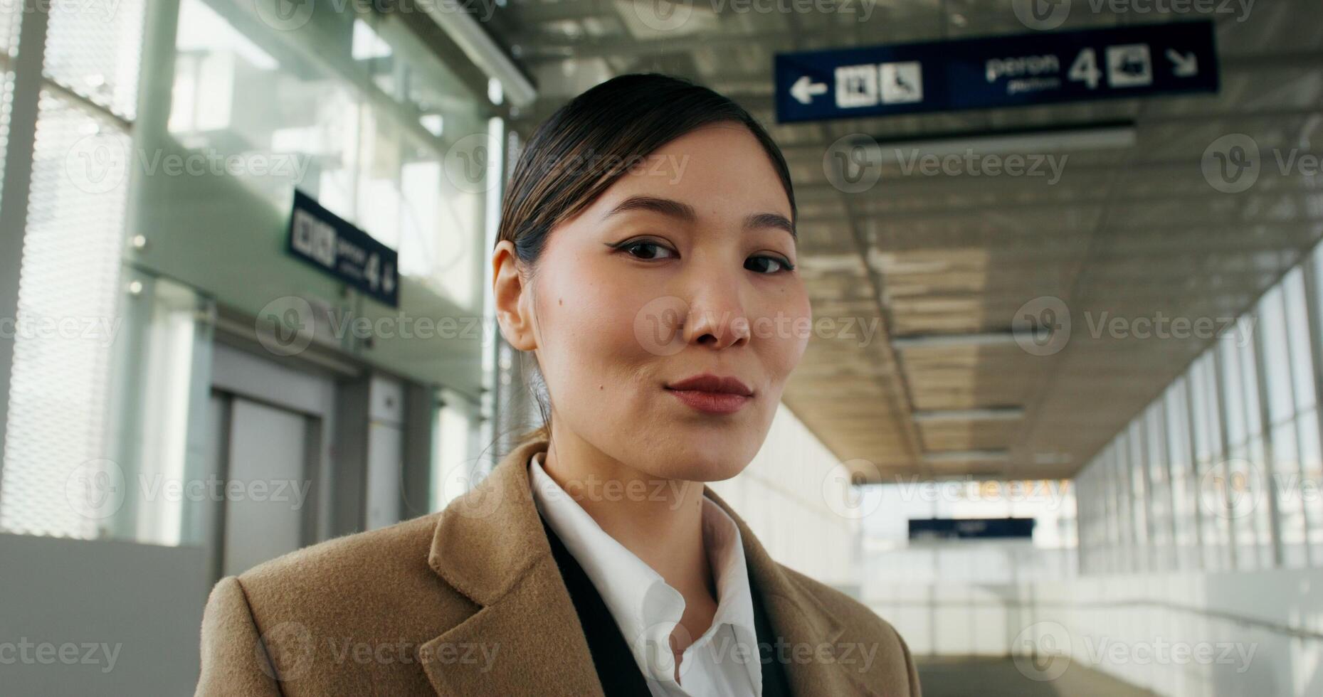 A woman in formal clothes smiles looking at the camera standing at the railway station, close-up of her face photo