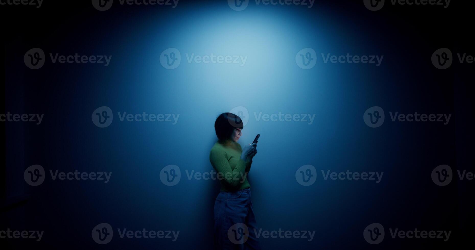 A woman in a wig uses a mobile phone, leaning against the wall in the blue backlight in the studio photo