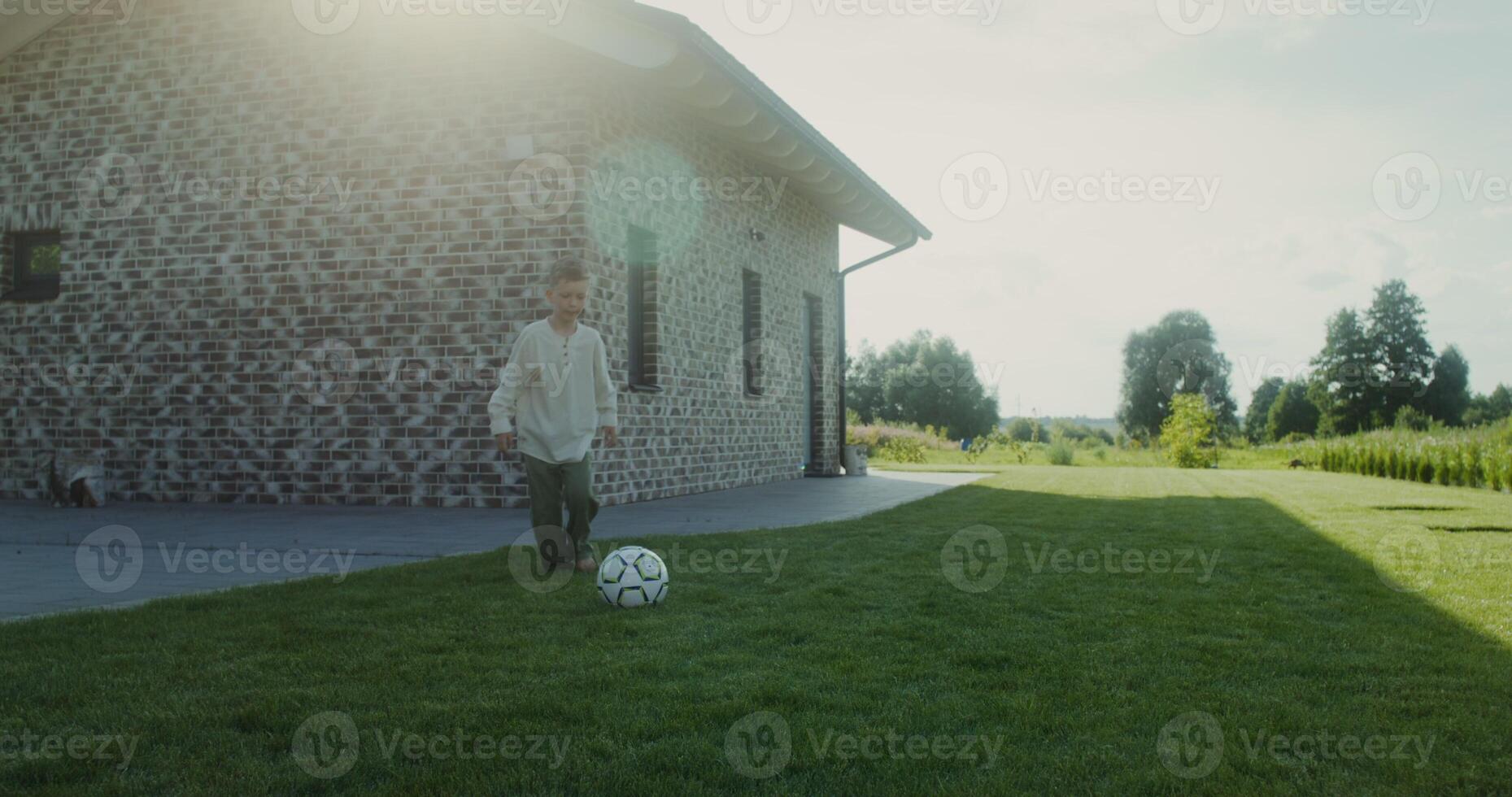 Boy having fun playing with a soccer ball in the backyard barefoot, summer evening photo