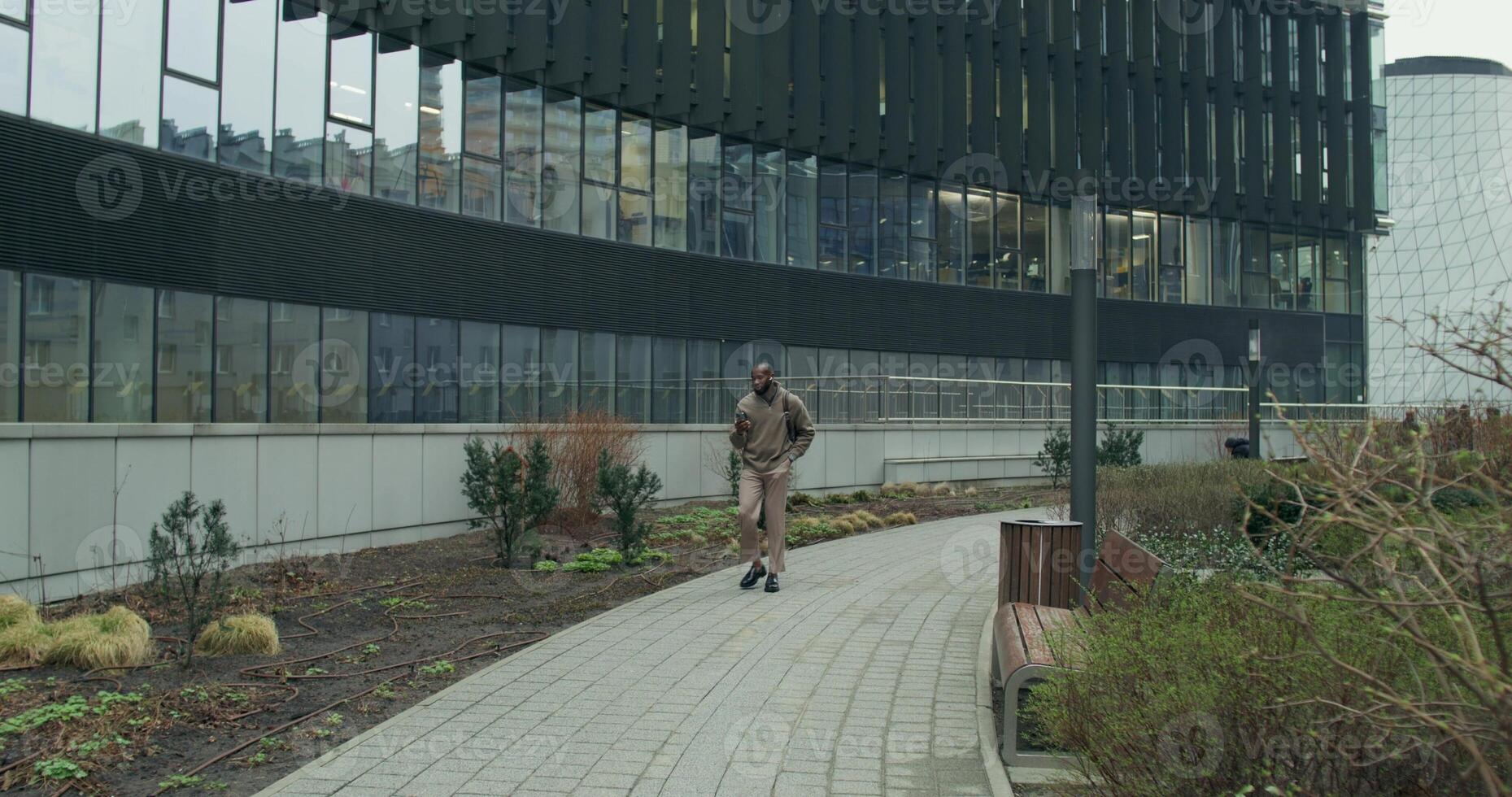 A man with earphones is talking on a chat on a mobile phone walking near a city skyscraper photo