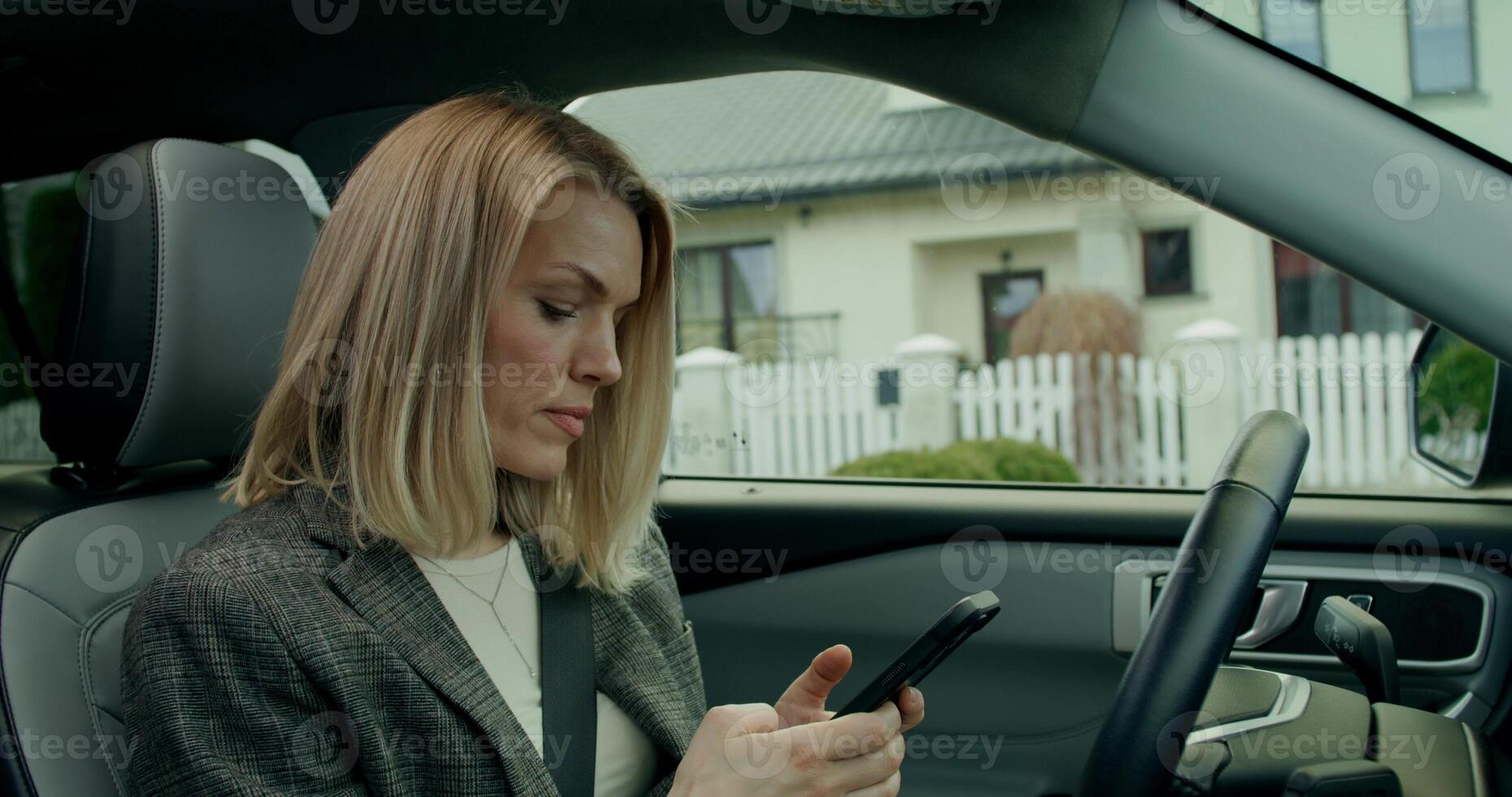 A stylish woman uses a mobile phone sitting in the driver's seat of a car while parking photo