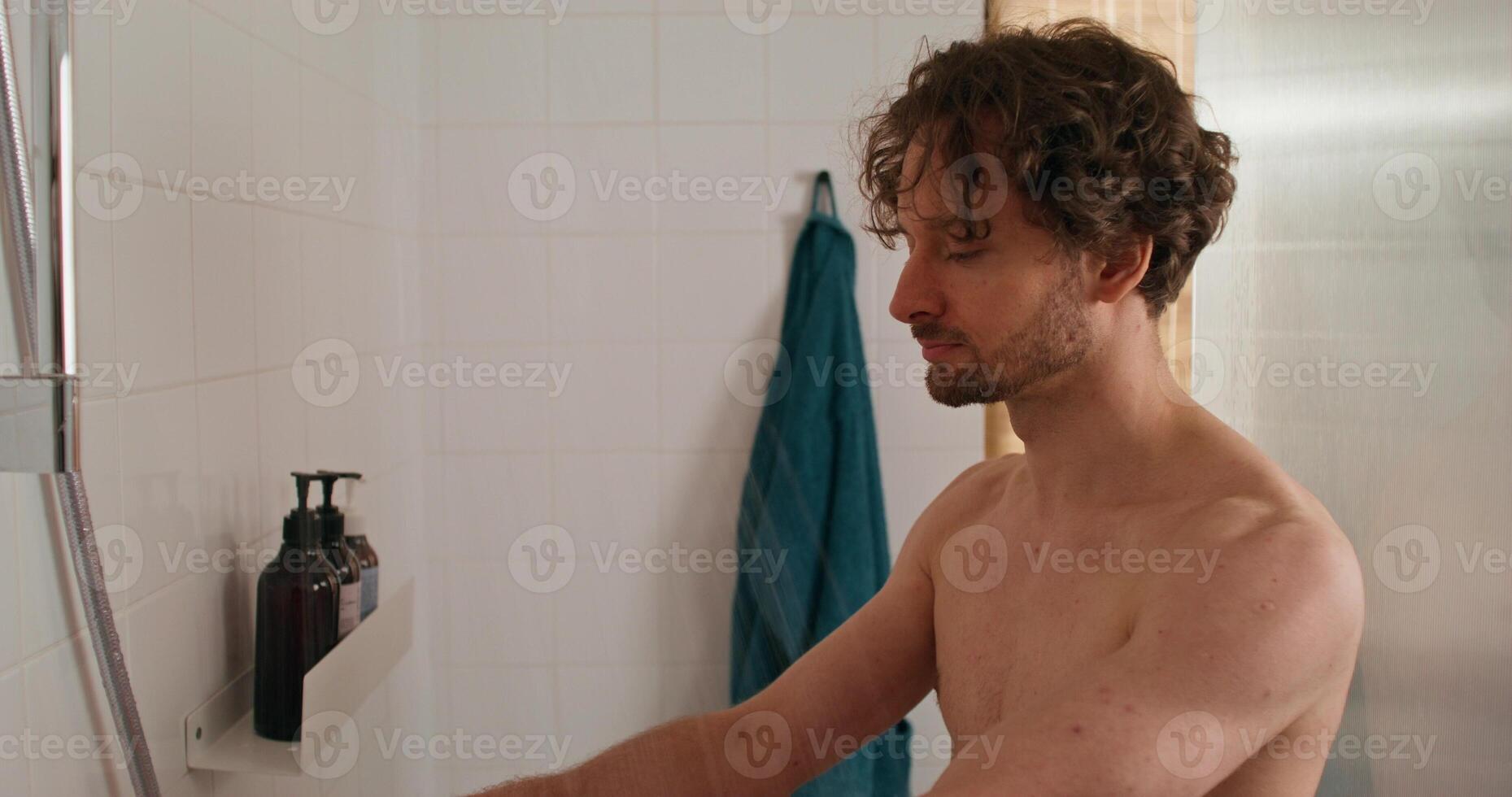 A man washes in the shower. He adjusts the water and gets under the water flow photo
